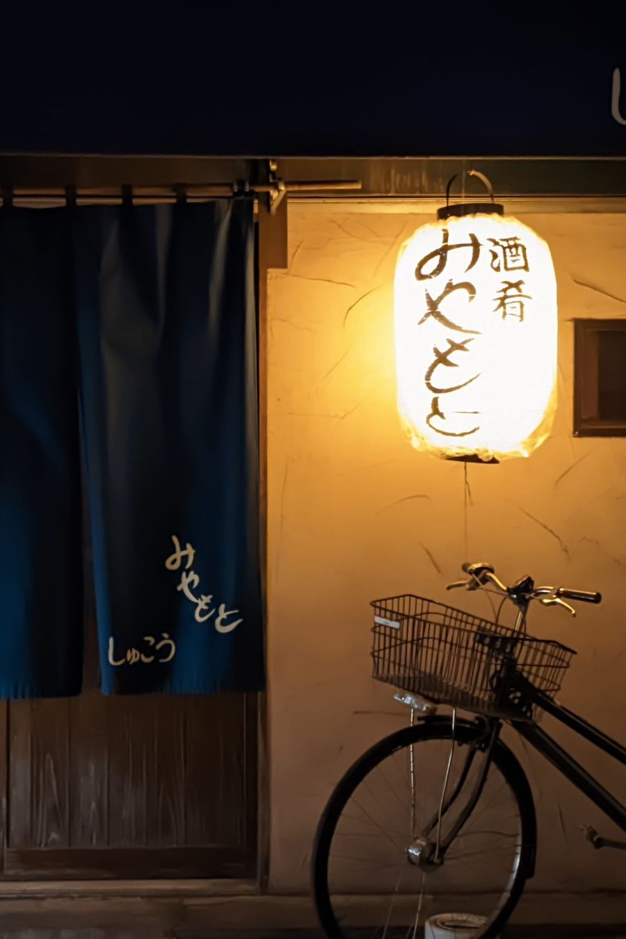 Entrada de un pequeño restaurante japonés con noren y farol encendido